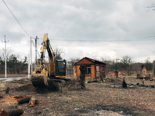 Fototapeta premium Excavator uprooting trees on land in countryside. Bulldozer clearing land from old trees and branches with dirt and trash. Backhoe machinery. Yard work