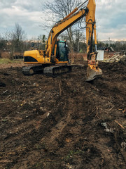 Excavator uprooting trees on land in countryside. Bulldozer clearing land from old trees, roots and...