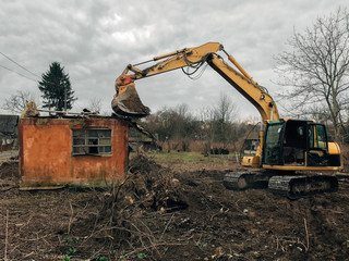 Excavator destroying brick house on land in countryside. Bulldozer clearing land from old bricks...