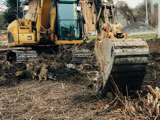 Excavator uprooting trees on land in countryside. Bulldozer clearing land from old trees, roots and...