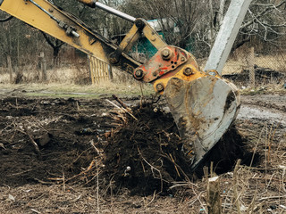 Excavator uprooting trees on land in countryside. Bulldozer clearing land from old trees, roots and...
