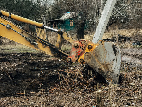 Excavator Uprooting Trees On Land In Countryside. Bulldozer Clearing Land From Old Trees, Roots And Branches With Dirt And Trash. Backhoe Machinery. Yard Work