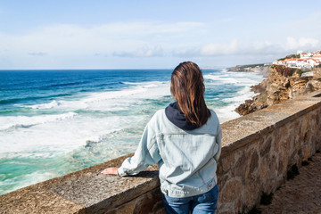 Fototapeta na wymiar Young girl looking at the panoramic view of beautiful houses on a rocky cliff at the coastal village of Azenhas Do Mar. Portugal