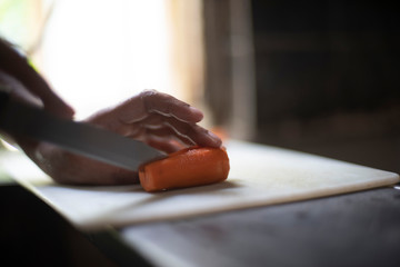 Woman cutting carrot with a knife on a chopping board in an Indian kitchen