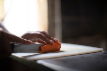 Woman cutting carrot with a knife on a chopping board in an Indian kitchen