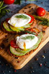Toast with poached eggs, tomatoes, avocado, spices and herbs. Tasty breakfast on the table