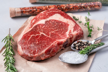 Raw rib eye steak on a light background with cooking ingredients, close up