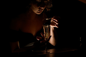 attractive girl at dark bar holds teaspoon over glass with cocktail