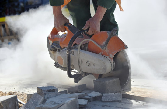 A Man Saws A Road Curb, Works On Road Construction.