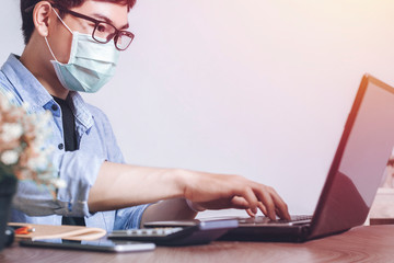Asian man wear a mask to protect against Corona virus. New normal Working using laptop in modern office. Small business company owner, startup entrepreneur, or working man lifestyle concept