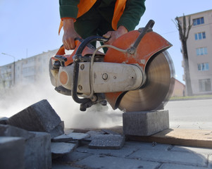 A worker with a circular saw cuts concrete tiles, a lot of dust.