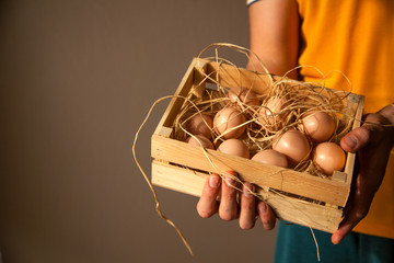 Male farmer holding a wooden box with hay and eggs in it. Warm background with copy space of a man holding eggs. Farming concept. Organic concept. Delivery concept. 