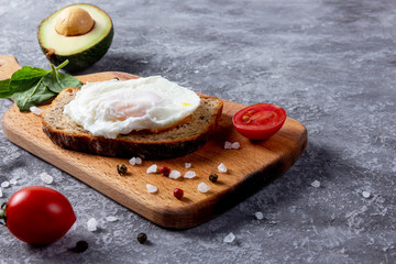 Toast bread with eggs, cherry tomatoes, avocado and greens on wooden cutting board