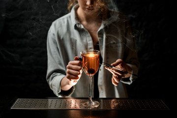 young woman bartender holds tweezers with smoking stick near wineglass