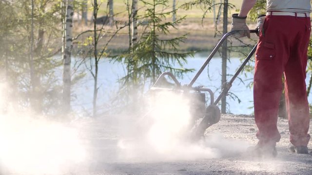 Man with stamper machine compacting soil for building foundation