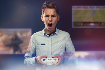 The concept of video games. Teen screams during video game. In the hands of holds joystick. Dark background. In front of his face transparent screens with video games