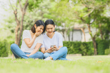 Fototapeta premium Two happy best friends Asian women are laughing while using mobile smartphone outdoor in the park