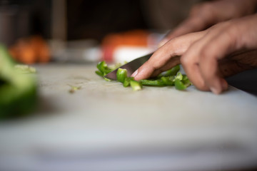 Woman chopping green capsicum with a knife on a chopping board in an Indian kitchen