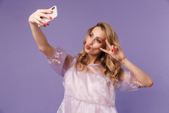 Image of woman gesturing peace sign and taking selfie on smartphone