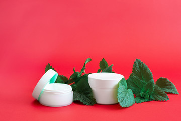 two white containers of cream with green branches on a red background
