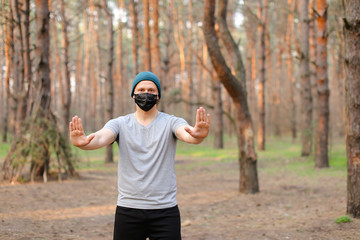 Young caucasian boy wearing mask and walking in park with stopping gesture.