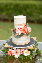 White wedding cake with orange and pink rose on it. Beautiful and rustic garden wedding setup on a sunny day during summer.