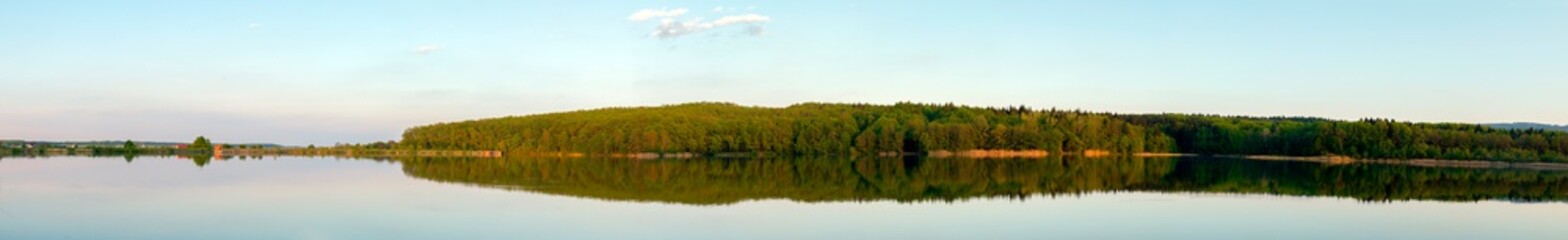 Panoramic landscape from the lake shore with colorful clouds in the spring sun.