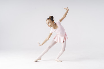 Delicate girl ballerina standing in ballet pose on white background in studio. Kinds personality...