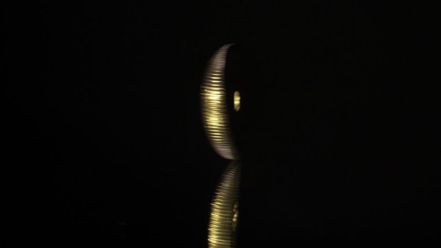 The 5 NOK coin rotates on a black mirror and a black background. Slow motion