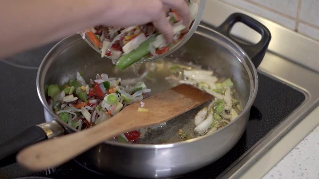 Pouring the vegetable mix over the onions in the pan