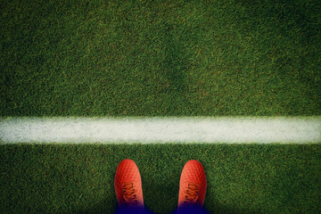 Top view of red soccer boots on the green field.