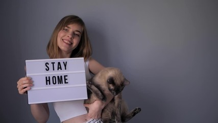 Attractive woman is advicing to stay at home during covid-19 pandemic. Woman is holding a cat in her arm. 