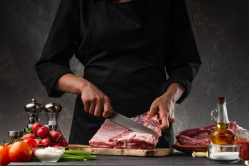 The chef cuts fresh pork ribs for cooking BBQ, on the background of vegetables. Cooking, recipe book, gastronomy. Butcher shop