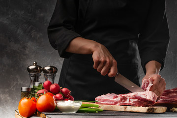 Slicing fresh meat, pork ribs on a background of fresh vegetables and a gray wall with space