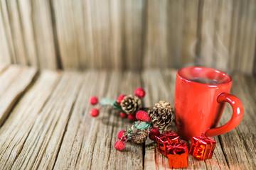 a red cup of coffee with Christmas ornament on the old wooden table top with wood panel background.