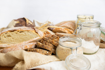 Heap of wheat ears, loafs and baguettes cut in slices, flour in jars, sackcloth. Closeup shot. Bakery or traditional bread concept