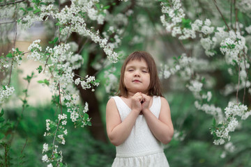 Cute tender Caucasian young girl with closed eyes near a flowering tree, a child with cherry blossoms. Concept of spring, freedom and tenderness.