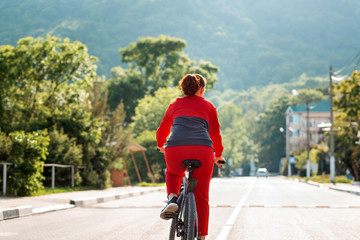 Sports lifestyle. A young woman in sports clothes, riding a Bicycle on an empty road. Rear view
