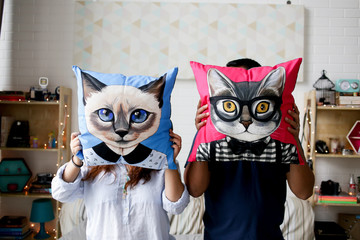 a couple holding a pillow with cat cover to hide their face