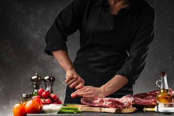 The chef cuts fresh pork ribs for cooking BBQ, on the background of vegetables. Cooking, recipe book, gastronomy. Butcher shop