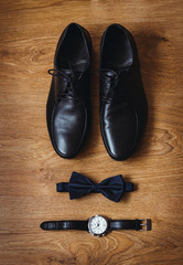 The groom is gathering in the morning. Wedding details. Men's watches. Leather men's shoes with bow tie. Set of groom accessories on wedding day. Photo on a wooden floor. Top view
