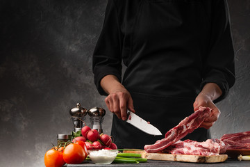 Slicing fresh meat, pork ribs on a background of fresh vegetables and a gray wall with space