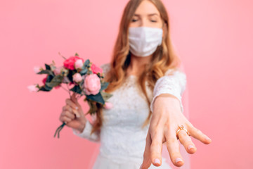 A bride in a wedding dress and a medical protective mask on her face on a pink background. Wedding, quarantine, coronavirus