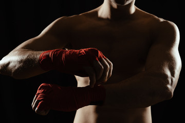 Close-up of the hands of a young boxer who winds red bandages before a match, fight or training.