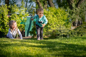 Fototapeta premium Two cute adorable playful caucasian blond children siblings little boy girl enjoy having fun playing together at home backtard green grass lawn at summer day. Brother sister happy childhood concept