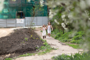 Fototapeta premium Tender young girls children jump and run near the blossoming cherry. Concept of spring, freedom and childhood. Authentic lifestyle, soft focus and sincere emotions