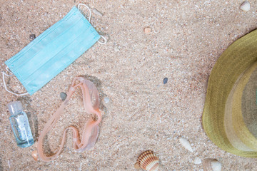 The concept of a background vacation trip with beach accessories and medical mask on a sand background at the time of the coronavirus pandemic. Top view with copy space.