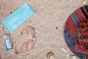 The concept of a background vacation trip with beach accessories and medical mask on a sand background at the time of the coronavirus pandemic. Top view with copy space.