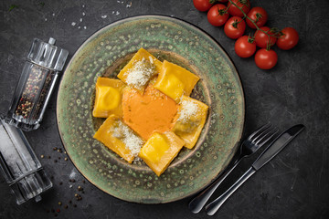 Yellow ravioli with cheese in a plate on a black background
