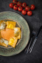 Yellow ravioli with cheese in a plate on a black background